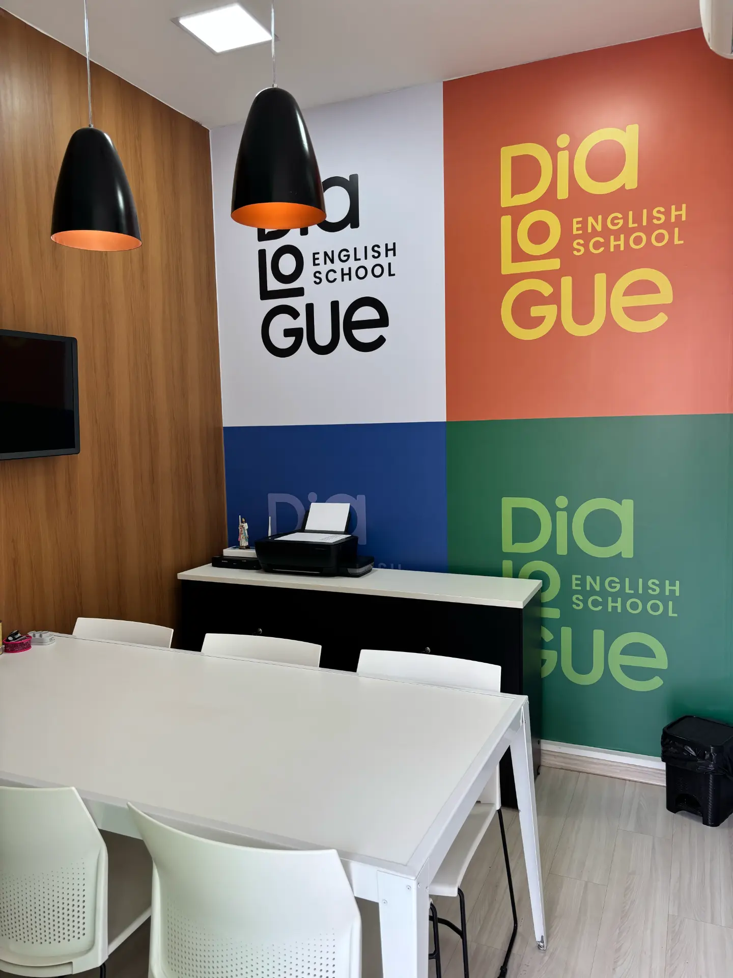 Sala de aula da Dialogue English School com mesa, cadeiras e painel da marca na parede
